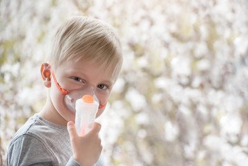 Blond boy in breathing mask inhaler on a background of flowering trees. Home treatment. Prevention