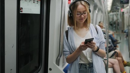 Modern young girl rides the subway and listens to music on headphones. Use a smartphone in the subway. Metro de Barcelona - Powered by Adobe