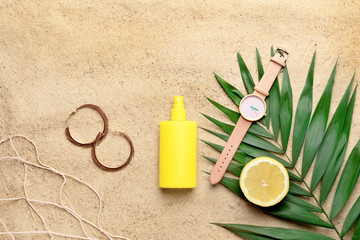 Bottle of sun protection cream and female accessories on sand