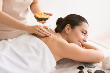 Obraz na płótnie Canvas Young woman undergoing treatment with body scrub in spa salon