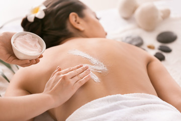 Young woman undergoing treatment with body scrub in spa salon