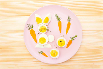 Easter bunny (rabbit) and chicken eggs children (kids) food concept. With carrot on rosy (pink) plate. Wooden background, top view