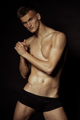 Fototapeta premium Strong stripped muscle male model in black underwear on black isolated font background