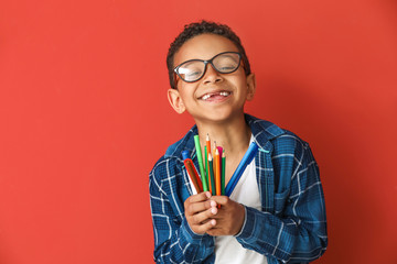 Cute African-American boy with pencils and markers on color background