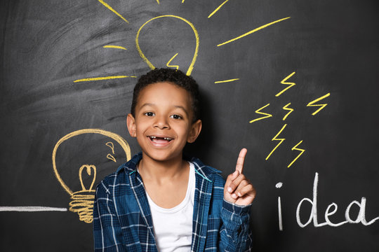 African-American boy with raised index finger near drawn light bulbs on dark wall