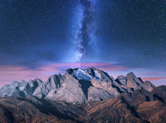 Milky Way over mountains in fog at night in summer. Landscape with alpine mountain valley, purple...