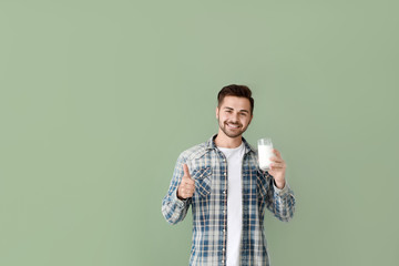 Handsome man with glass of tasty milk showing thumb-up gesture on color background