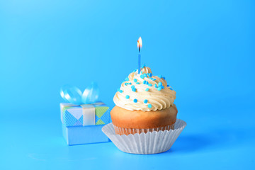 Tasty Birthday cupcake with gift box on color background