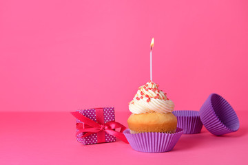 Tasty Birthday cupcake with gift box on color background