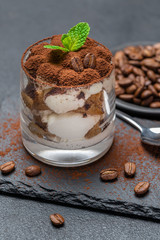 Classic tiramisu dessert in a glass on stone serving board on dark concrete background