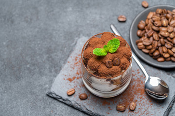Classic tiramisu dessert in a glass on stone serving board on dark concrete background