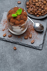 Classic tiramisu dessert in a glass on stone serving board on dark concrete background