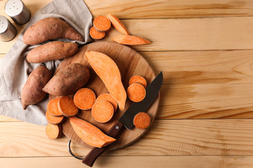 Cutting board and knife with raw sweet potato on wooden background