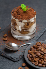 Classic tiramisu dessert in a glass on stone serving board on dark concrete background