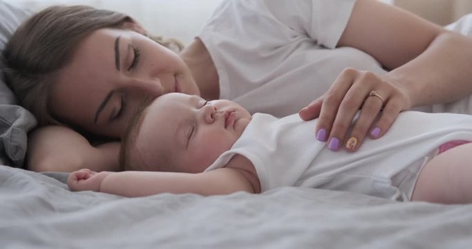 Happy mother gently stroking and kissing her adorable sleeping baby girl in bed