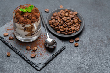 Classic tiramisu dessert in a glass on stone serving board on dark concrete background