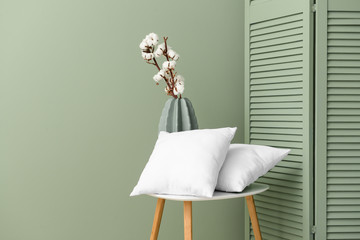 Table with soft pillows and vase with cotton flowers near color wall