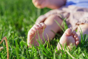 Cute little girl sits on the green grass, outdoors, summer time, blurred background