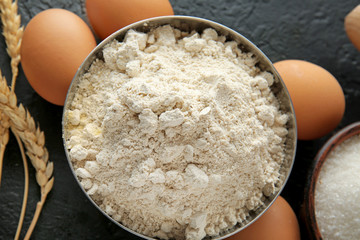 Bowl with flour and products on dark background