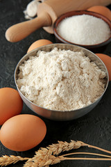 Bowl with flour and products on dark background