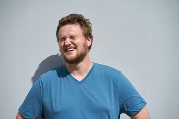 Caucasian bearded young man in blue t-shirt laughing in sunlight with closed eyes