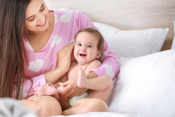 Fototapeta na wymiar Happy mother with adorable baby boy sitting on bed at home
