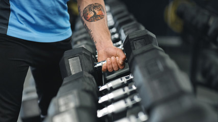 Fototapeta na wymiar Muscular male arm picking up heavy dumbbell from equipment rack