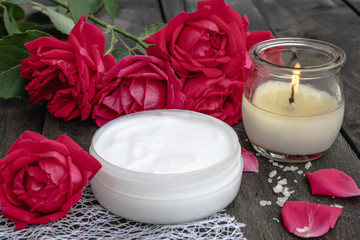 cosmetic cream and roses with petals and a burning candle on the old wooden background.