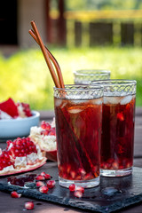 Refreshing summer cold drink, outdoors. Pomegranate juice with ice and broken pomegranate on a wooden garden table.
