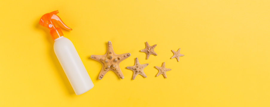 Sunscreen Bottles With Seashells On Yellow Table Top View