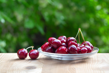 Cherry on a glass platter on the background of greenery. Green blurred background with bokeh. Bright sunny day. Juicy, tasty, healthy fruits.