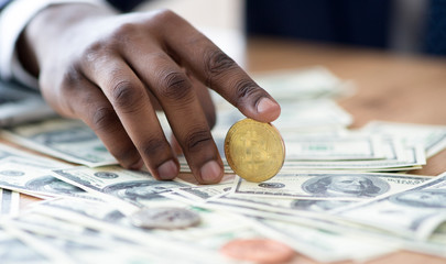 Black businessman holding golden BTC coin on stack of dollars