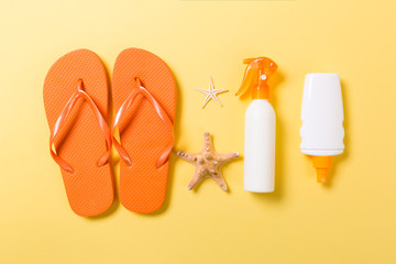 Sunscreen bottle or body spray on yellow background top view flat lay with copy space. Holiday vacation travel concept with beach sea accessories