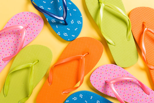 many colored flip flops on yellow background. Copy space top view