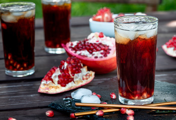 Refreshing summer cold drink, outdoors. Pomegranate juice with ice and broken pomegranate on a wooden garden table.