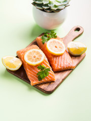 Salmon fillet on wooden board with lemon slices, parsley and pink salt. Pastel green background. Healthy fish meal to be cooked. Protein source.