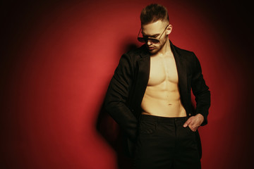 Obraz premium Muscle strong face beautiful stripped male model in casual look with denim and suit wearing glasses on bordo red isolated font background