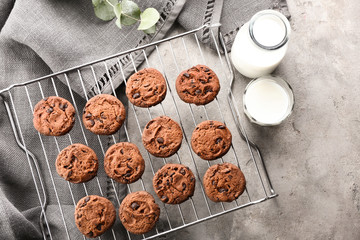 Cooling rack with tasty chocolate cookies and milk on grey background