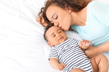 Happy African-American mother with cute little baby in bedroom
