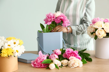 Female florist working with beautiful peonies on grey background