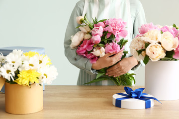 Female florist with beautiful bouquet of peonies on grey background