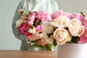Female florist with beautiful bouquet of peonies on grey background