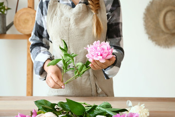 Woman making bouquet of beautiful peonies at table