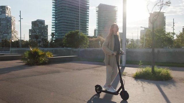 Young beautiful woman riding an electric scooter to work, modern girl, new generation, electric transport, ecology, ecological transport, sunset, electric skateboard, 4k