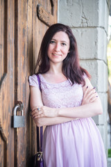 Fototapeta premium Young happy smiling caucasian woman in a summer dress leaning against the door outdoors