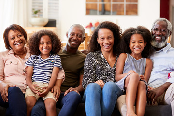 Fototapeta premium Portrait Of Smiling Multi-Generation Family Sitting On Sofa At Home Relaxing Together