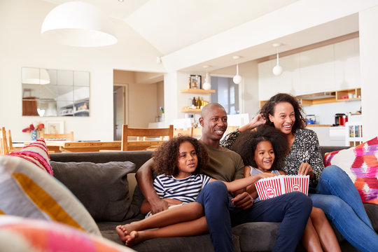 Family Sitting On Sofa At Home Eating Popcorn And Watching Movie Together