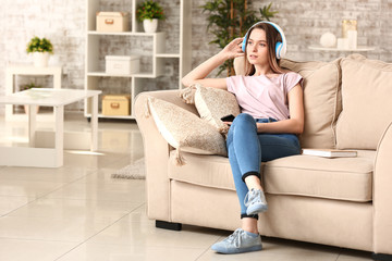 Beautiful young woman listening to audiobook while sitting on sofa at home