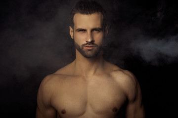 Fototapeta na wymiar Handsome sport sexy stripped guy portrait in a water draps and fog smoke mist on isolated black background