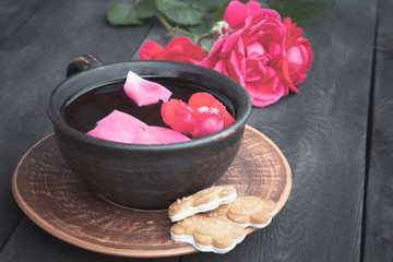 on a saucer a cup of tea of red rose petals on a wooden background.